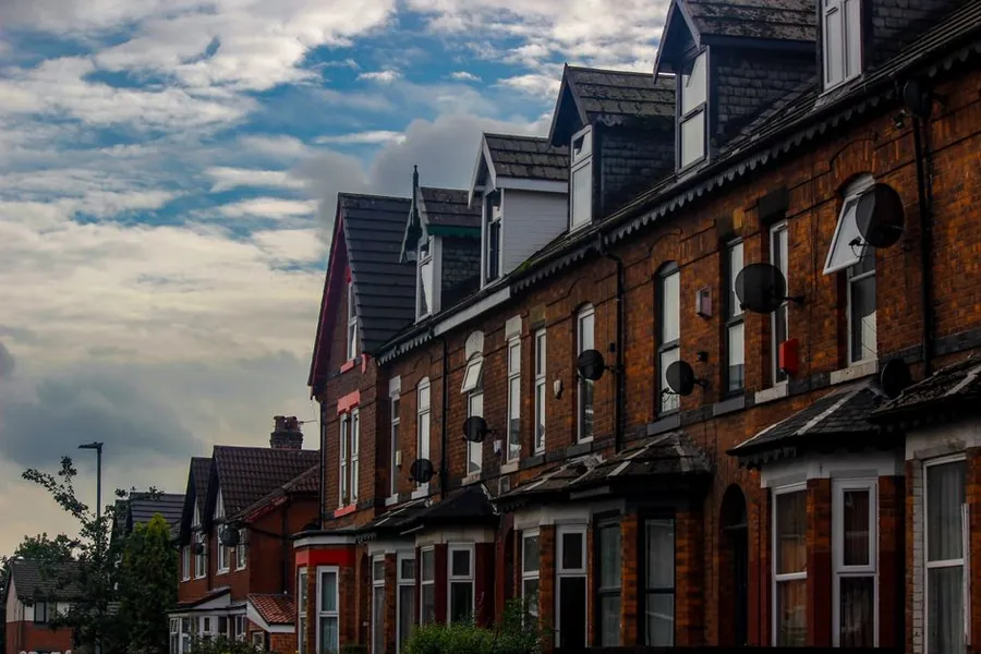 Row of red brick terraced houses with shared party walls under a cloudy British sky
