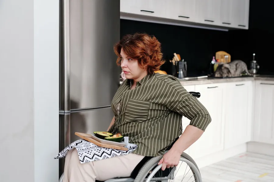 Wheelchair user preparing food at an accessible kitchen worktop with clear space beneath