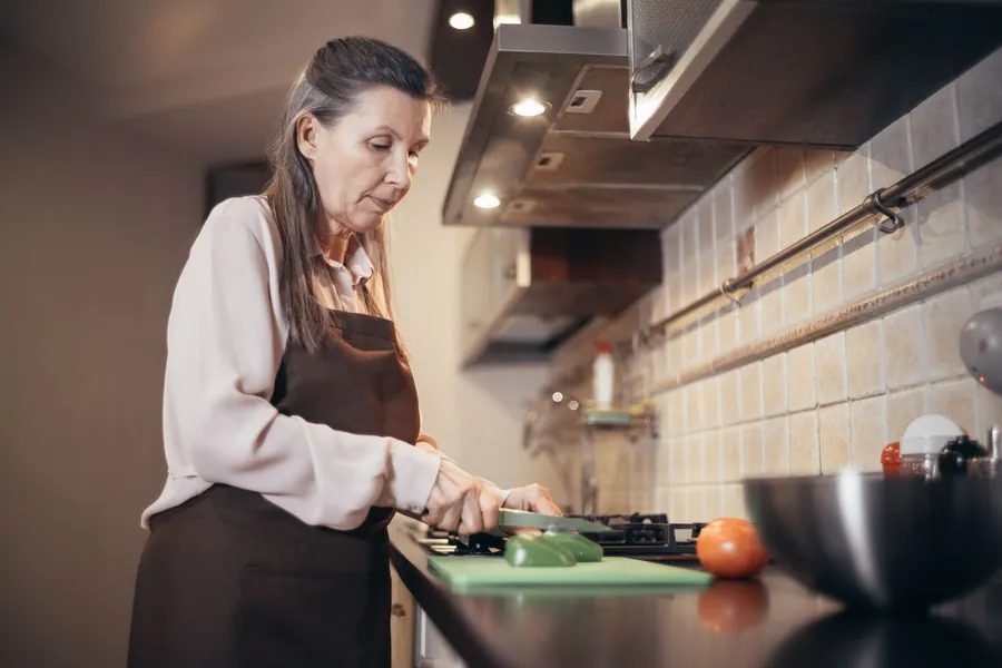 Older woman chopping vegetables at a kitchen worktop with good visible contrast in a Liverpool home