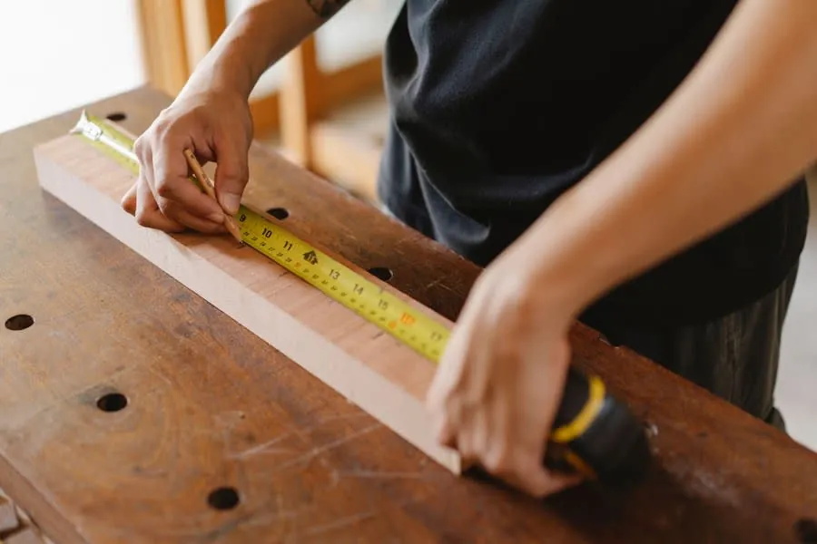Joiner measuring timber with a tape measure before cutting alcove shelving