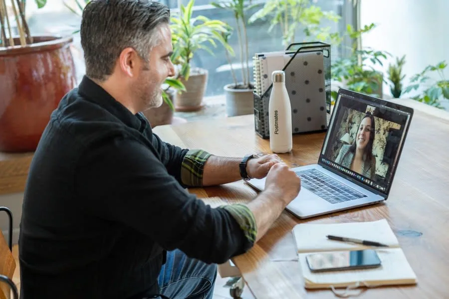 Person on a video call at a home office desk with shelving behind them