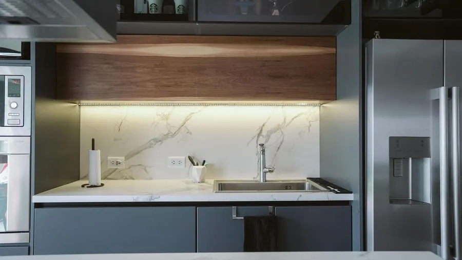 Modern kitchen with sleek cabinets, white marble backsplash, black countertop, and stainless steel refrigerator.