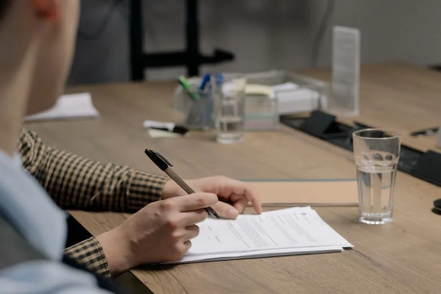 Person signing a written contract at a wooden table