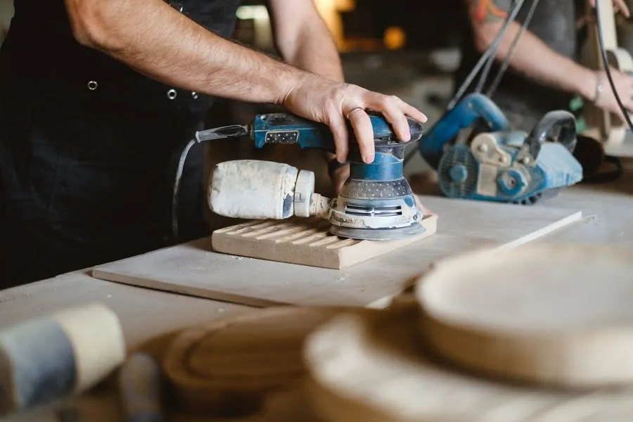 Joiner sanding and finishing a timber cabinet panel in a workshop