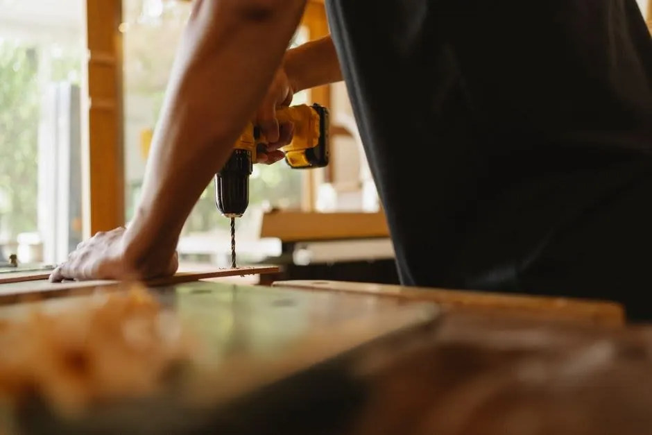 Joiner drilling into a timber panel while building kitchen cabinets in a workshop