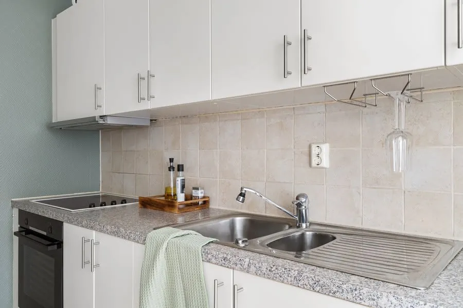 Modern kitchen counter with white cabinets, stainless sink, stovetop, and a towel draped over the counter