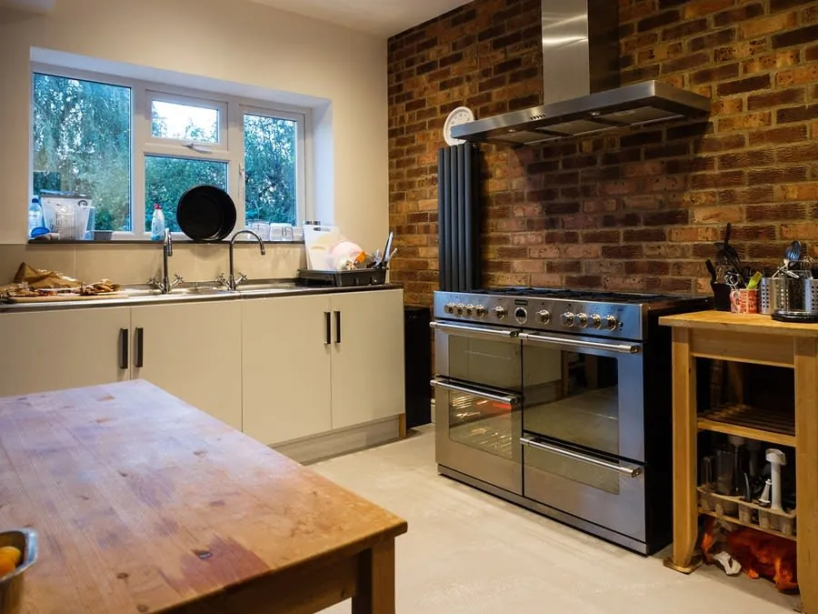 Modern kitchen with brick backsplash, white cabinets, stove, and wooden table by a window