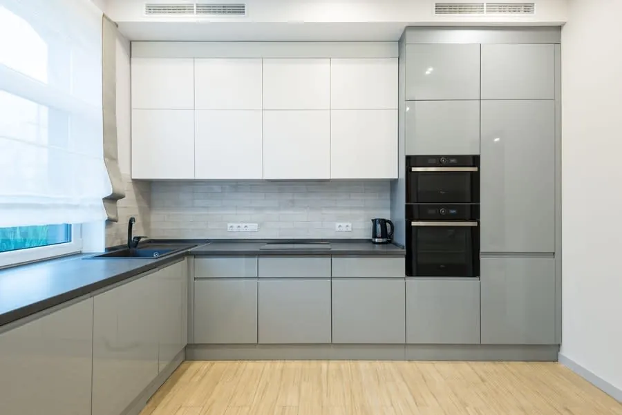 Modern minimalist kitchen with gray cabinets, white upper cupboards, black countertop, and wood floor.
