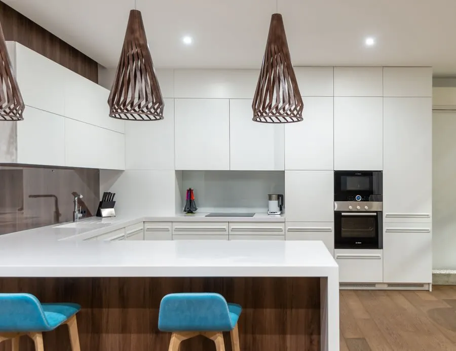 Modern white kitchen with island, blue stools, wood accents, and woven pendant lights