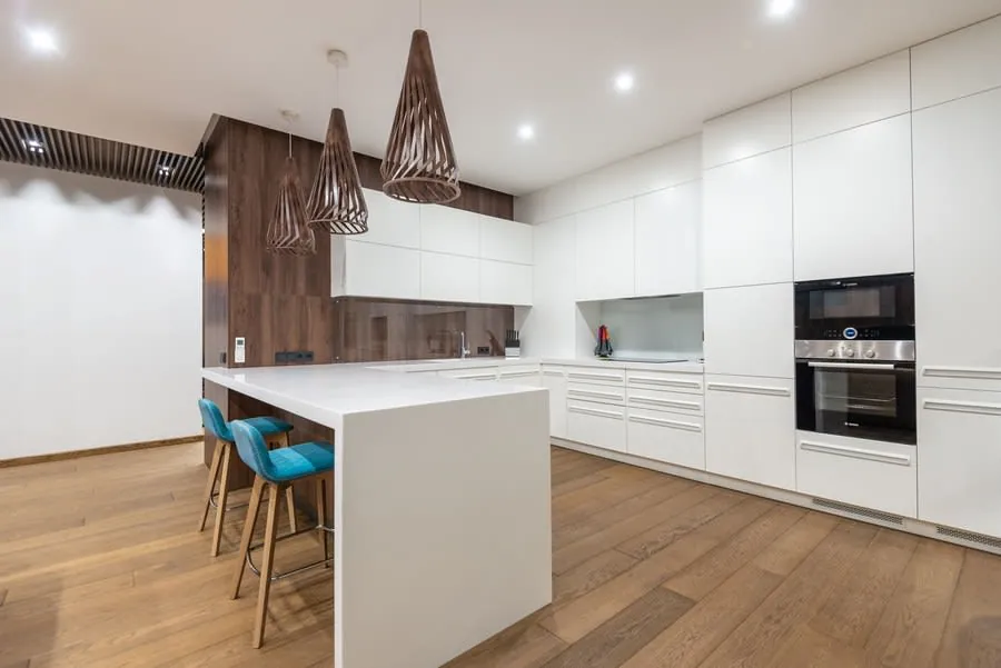 Modern white kitchen with wood accents, island seating, built-in appliances, and pendant lights