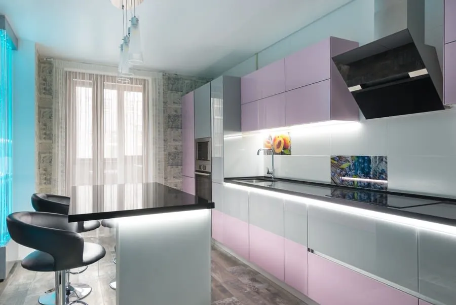 Modern kitchen with pastel pink cabinets, black island, and large window with sheer curtains