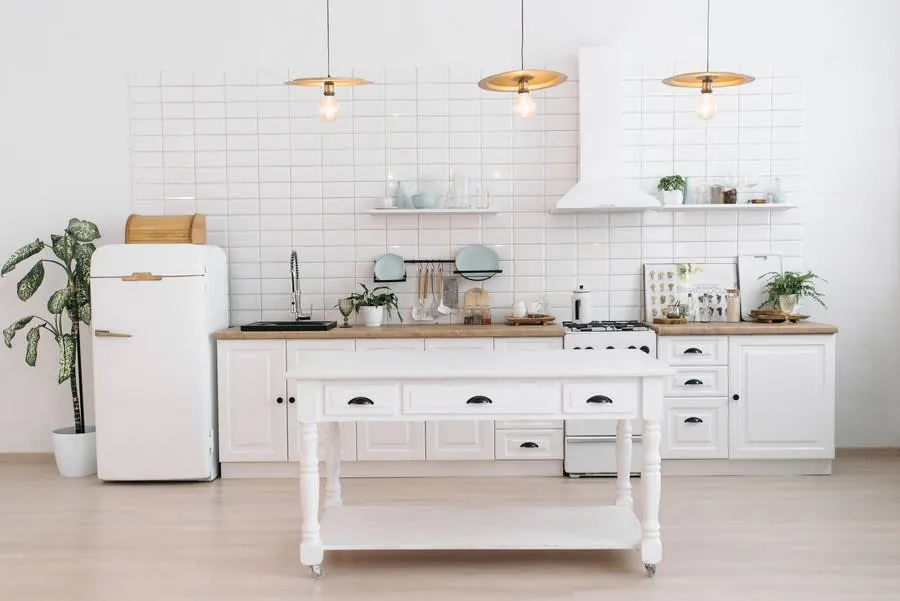 Minimal white kitchen with island, pendant lights, and a vintage refrigerator and desk on the left