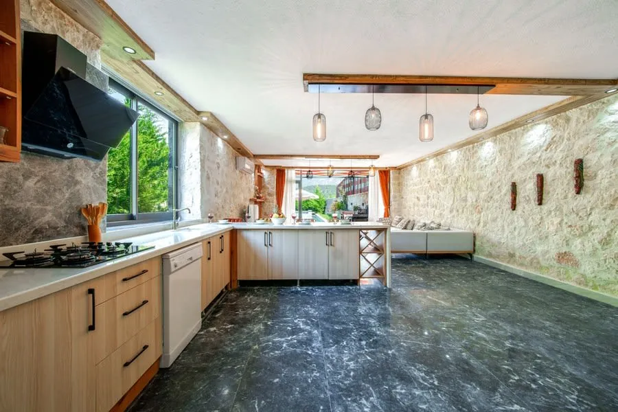 Modern kitchen with light wood cabinets, large windows, pendant lights, and dark flooring