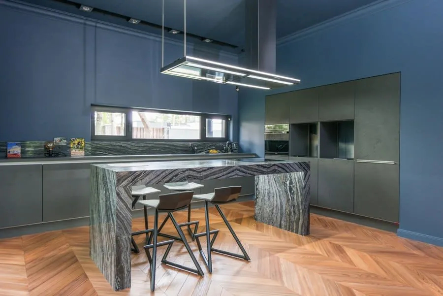 Modern kitchen with dark blue walls, marble island, bar stools, and pendant lights