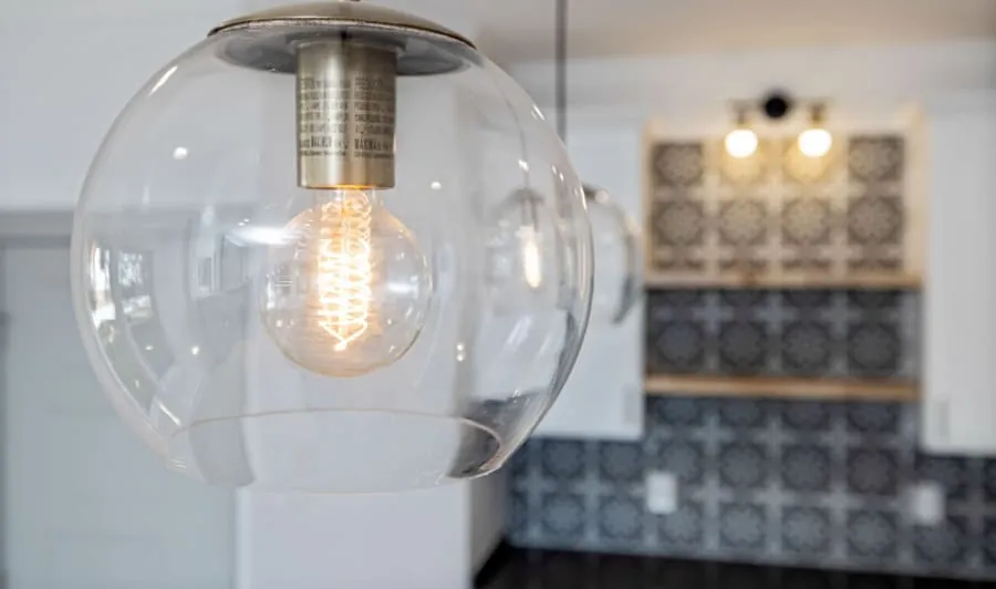 Clear glass pendant light hanging in a kitchen with patterned tile backsplash and blurred decor background