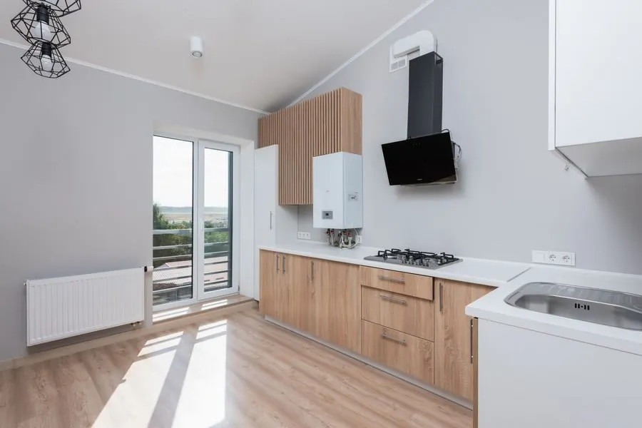 Empty kitchen with wooden cabinets and large windows awaiting a refit