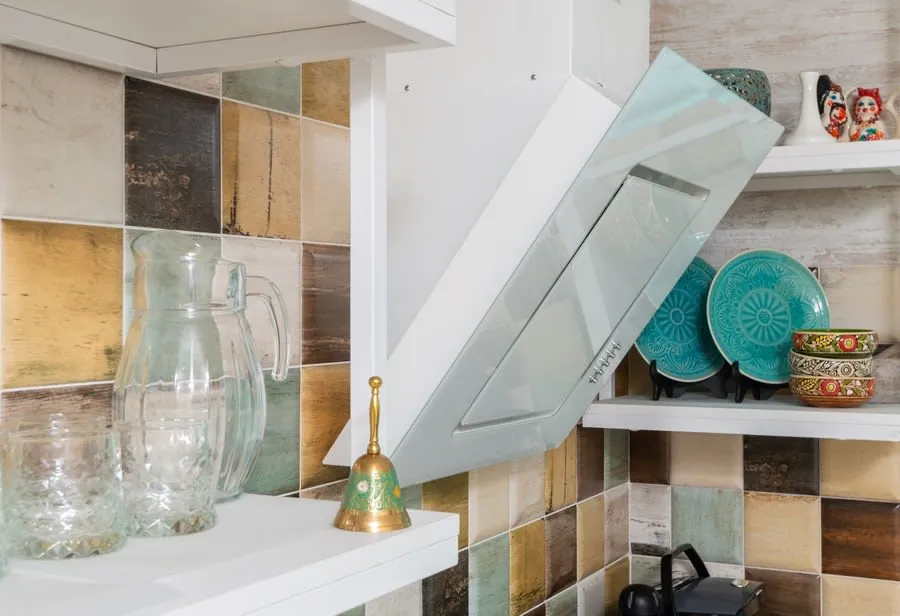 Kitchen shelf with glass jars, turquoise plates, and a small gold bell against a tiled backsplash