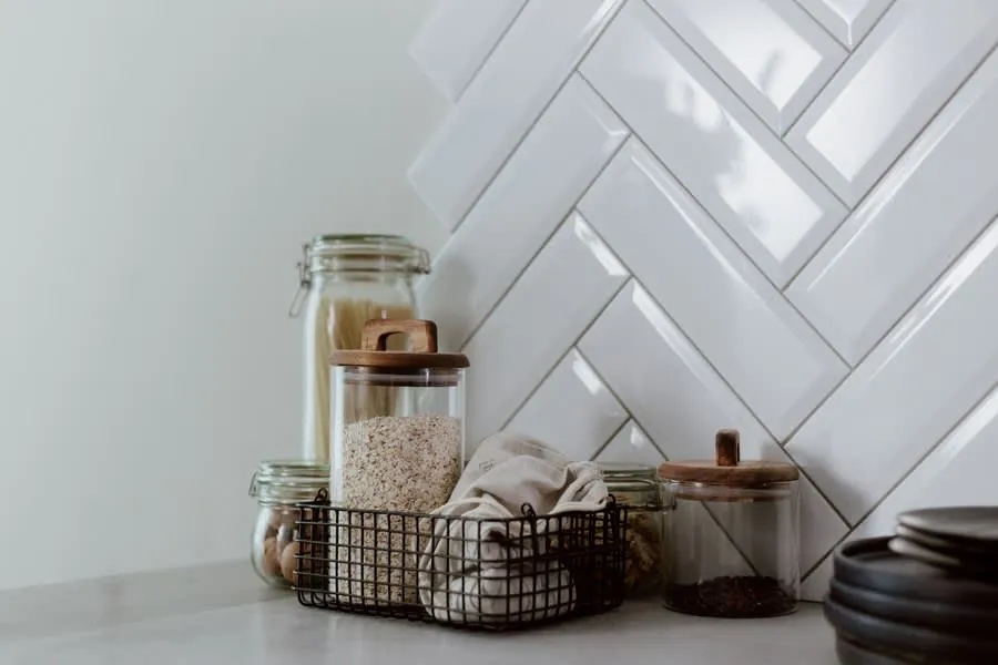 Glass jars and canisters on a kitchen counter against a white herringbone tile backsplash