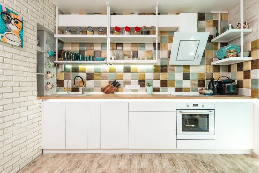 Bright modern kitchen with white cabinets, colorful tile backsplash, open shelves, and built-in oven