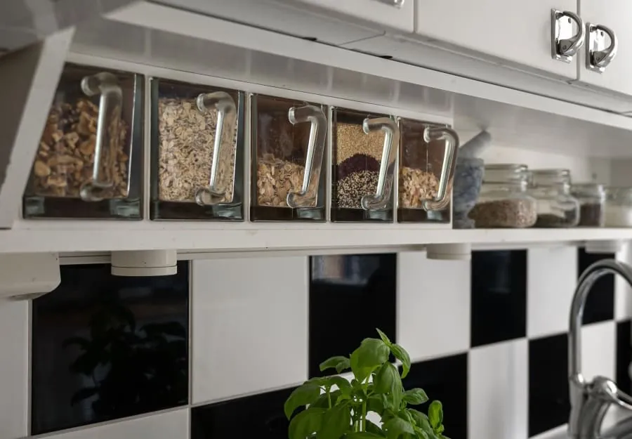 Kitchen shelf with labeled glass jars of dried goods above a black-and-white backsplash.