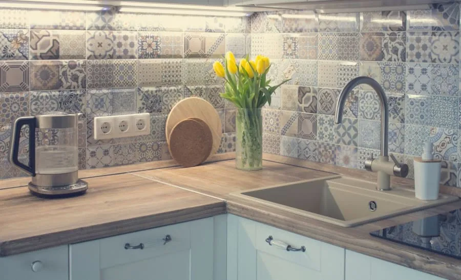 Bright kitchen counter with sink, patterned tile backsplash, yellow flowers, and a coffee machine