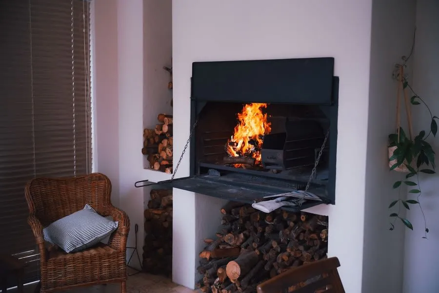 Wood burning stove with stacked logs and a wicker chair in a warm living room