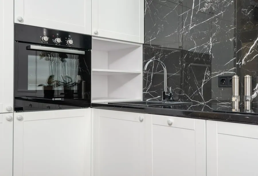 Modern white kitchen with black marble backsplash, built-in oven, and stainless sink