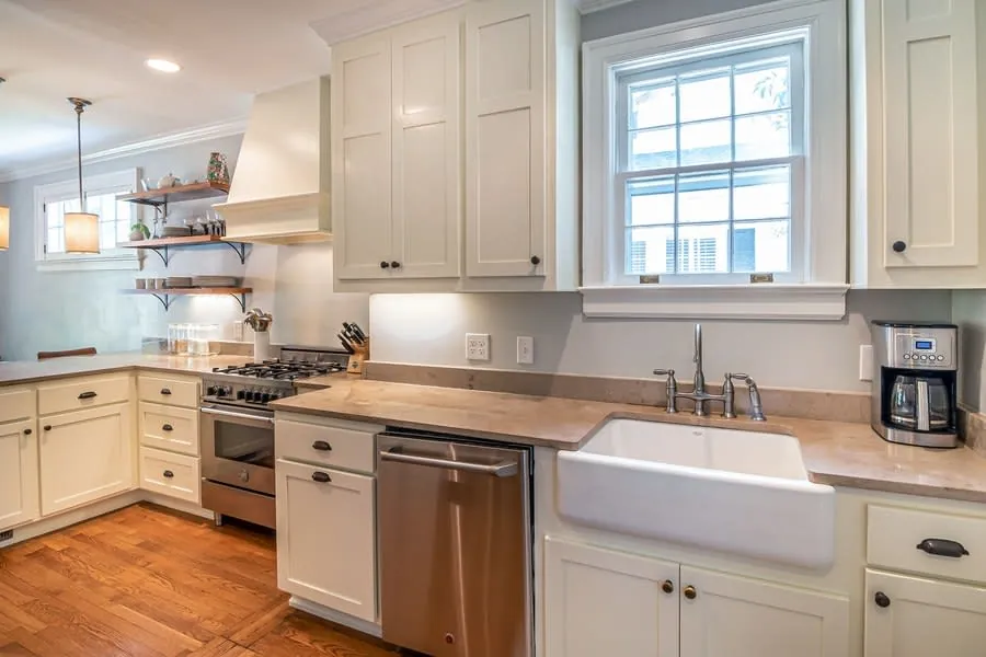Bright white kitchen with farmhouse sink, stainless stove, and wood floors