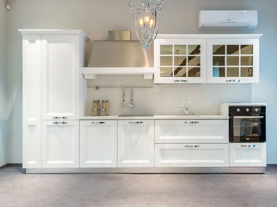 Modern white kitchen with cabinets, built-in oven, wall AC unit, and a central island under a pendant light
