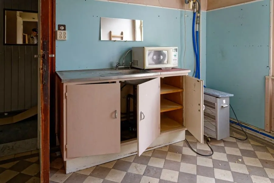 Worn kitchen cabinets with open doors showing the damage water does to unit carcasses
