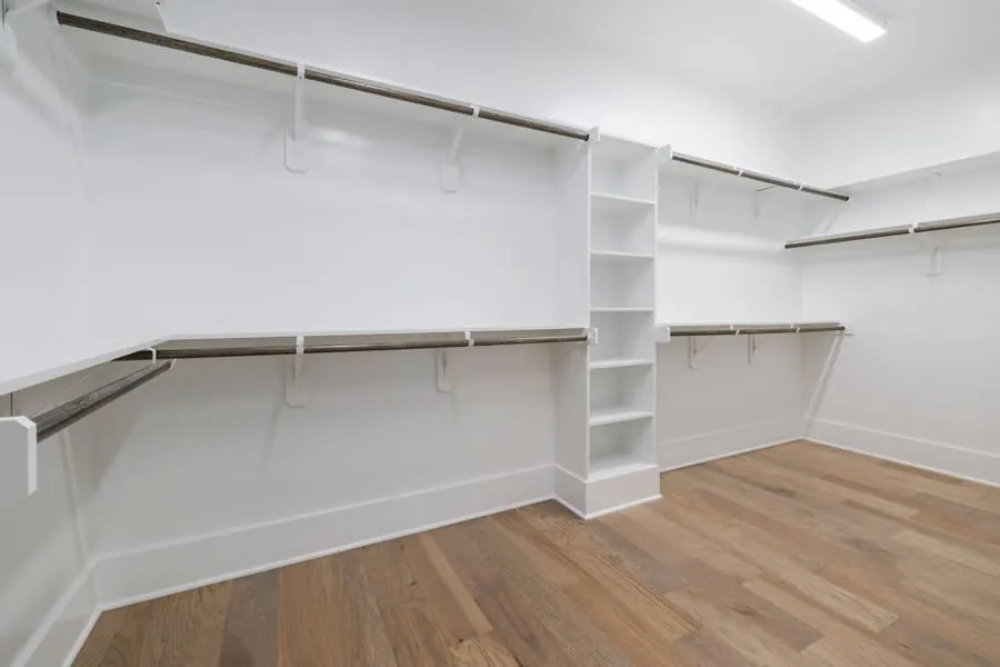 Empty walk-in wardrobe with white shelving and wooden flooring