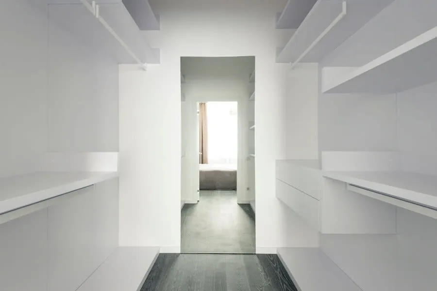 Bright minimalist walk-in wardrobe with open shelving down one wall