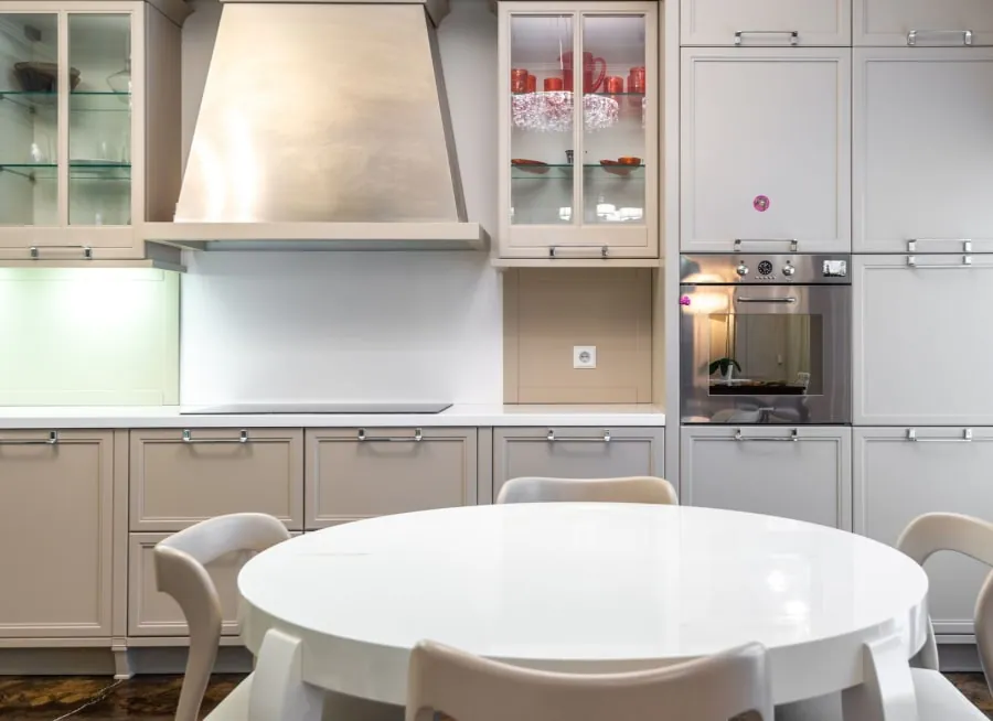 Modern kitchen with beige cabinets, stainless range hood, and a white round table in the foreground