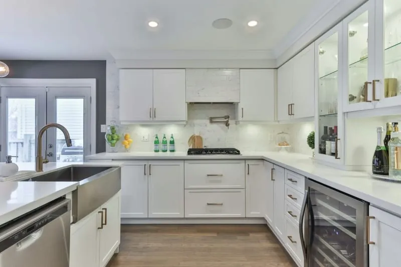 Modern white kitchen with stainless steel appliances, a wine fridge, and wooden floor.