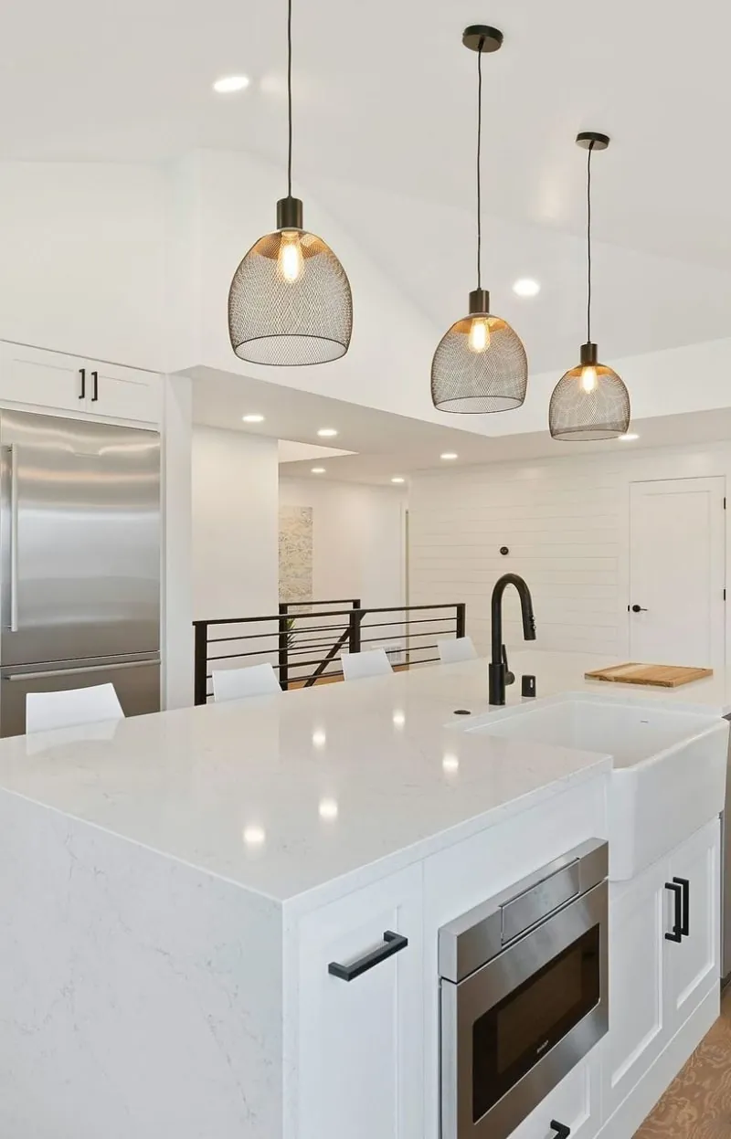 Modern white kitchen with an island, pendant lights, and built-in microwave.