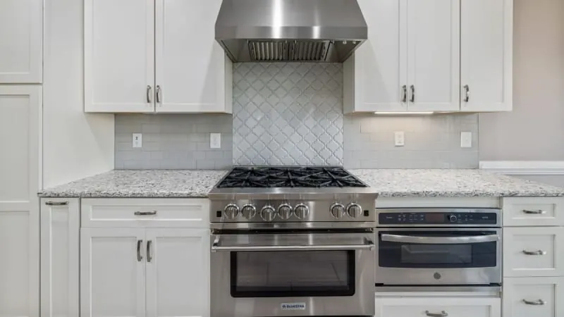 Stainless steel range and microwave in white kitchen with granite countertops and mosaic backsplash.
