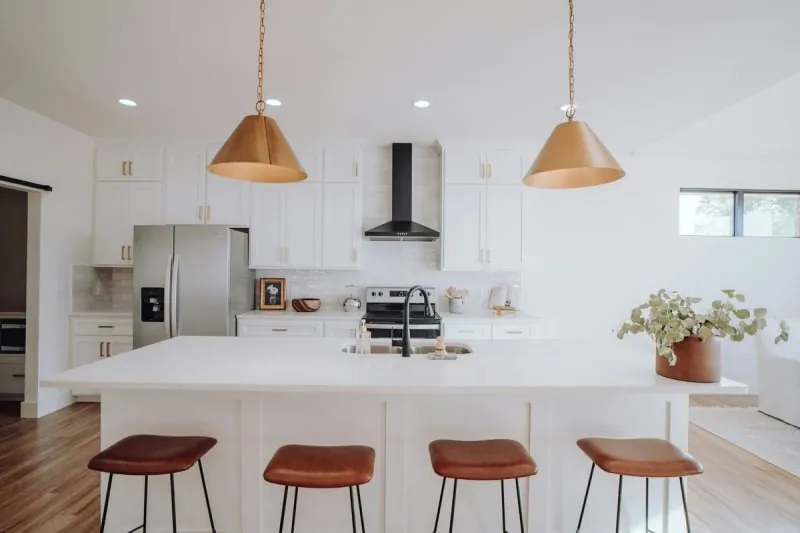 Modern white kitchen with an island, pendant lights, and brown leather stools.