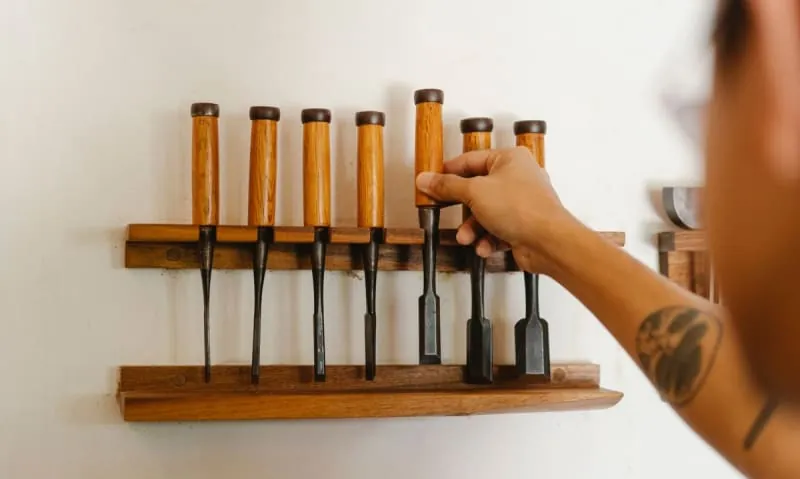 Joiner selecting a chisel from a tool rack in a joinery workshop