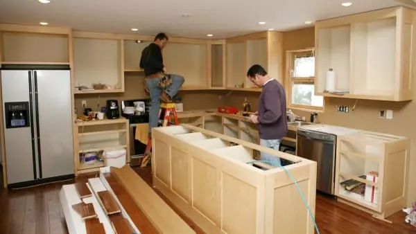 Two men installing kitchen cabinets in a newly renovated kitchen.
