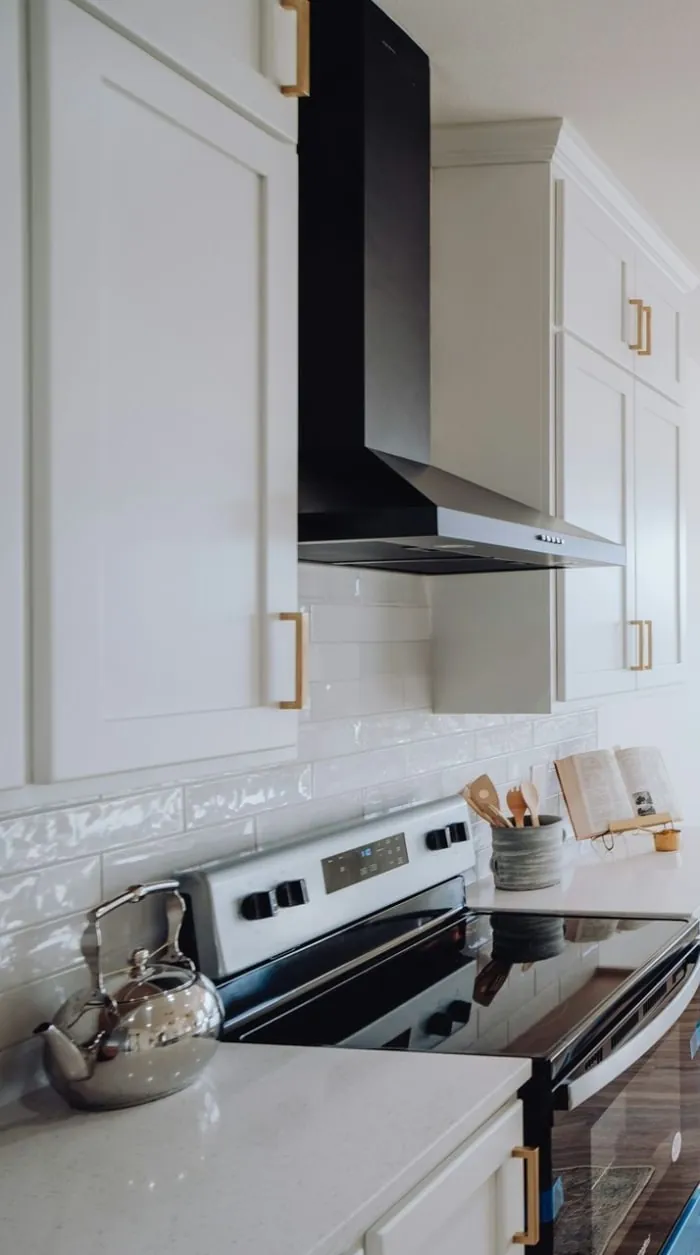 White kitchen with black range hood, cabinets, and stove. Gold hardware.