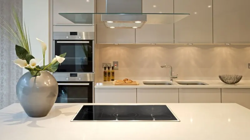 Modern kitchen with white cabinets, island with stovetop, silver vase, and stainless steel appliances.