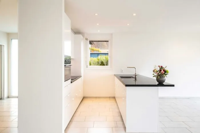 White modern kitchen with black countertop island, window, and floral arrangement.