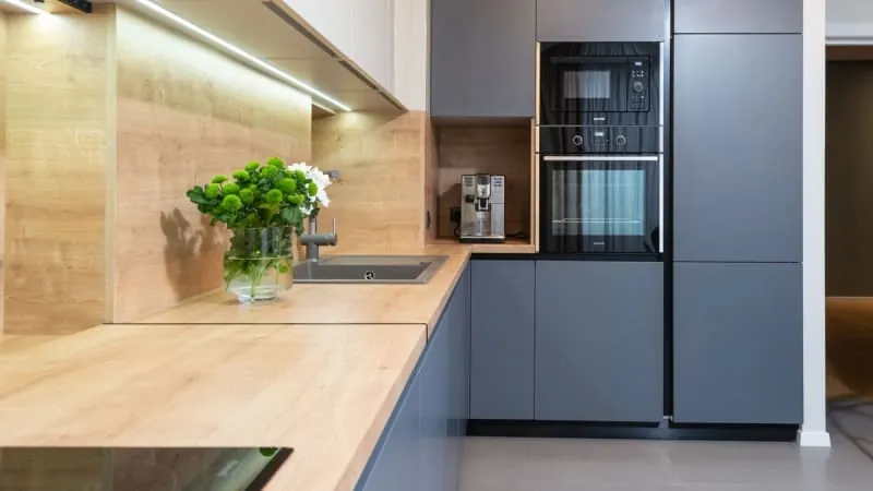 Modern kitchen with light wood and gray cabinets, built-in oven and microwave.
