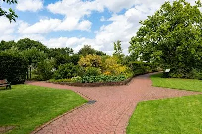 Brick pathways split in a green park with lush trees and a cloudy sky.